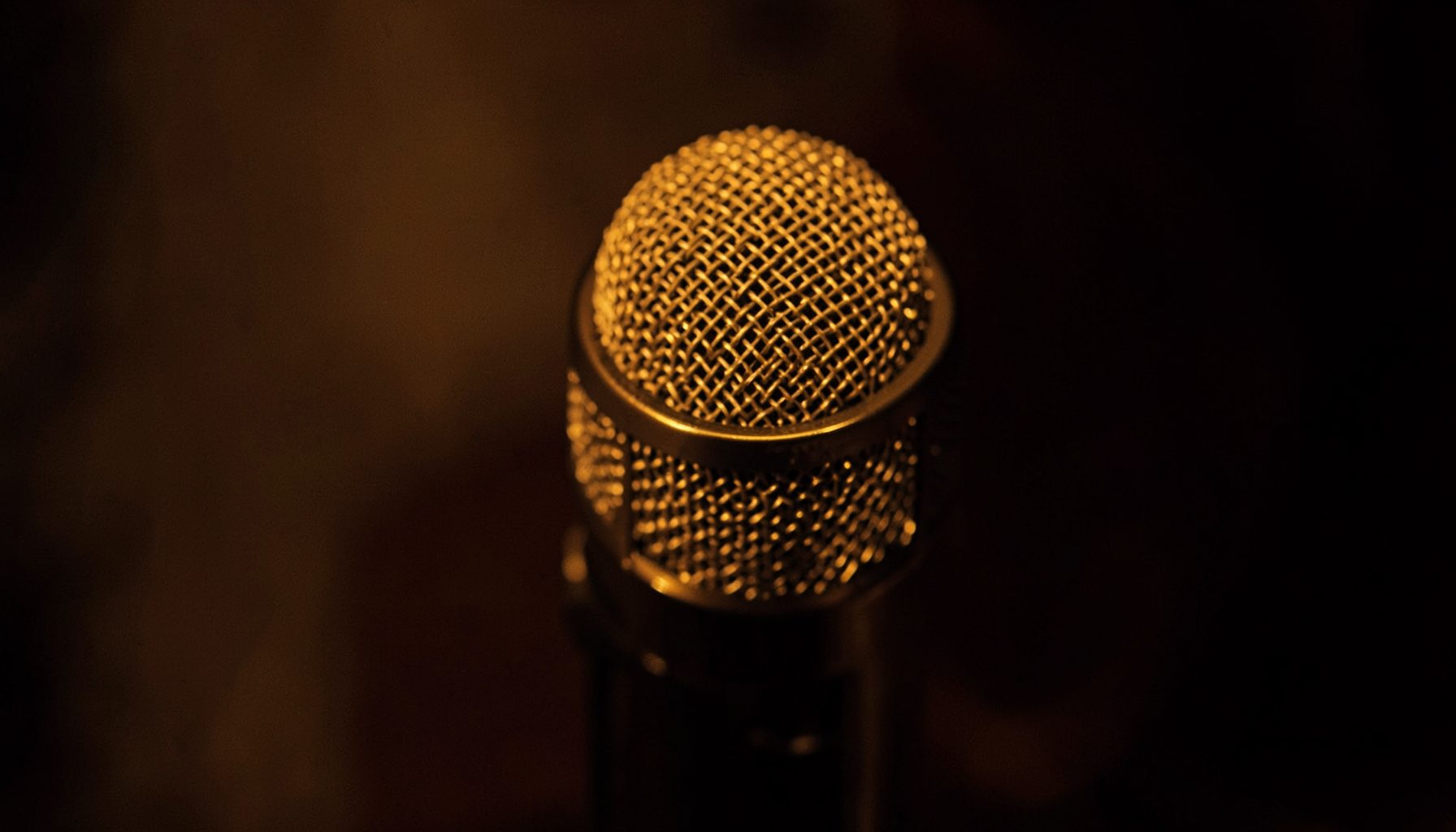 Close-up of a microphone head with metallic mesh lit in warm amber tones, moody atmosphere