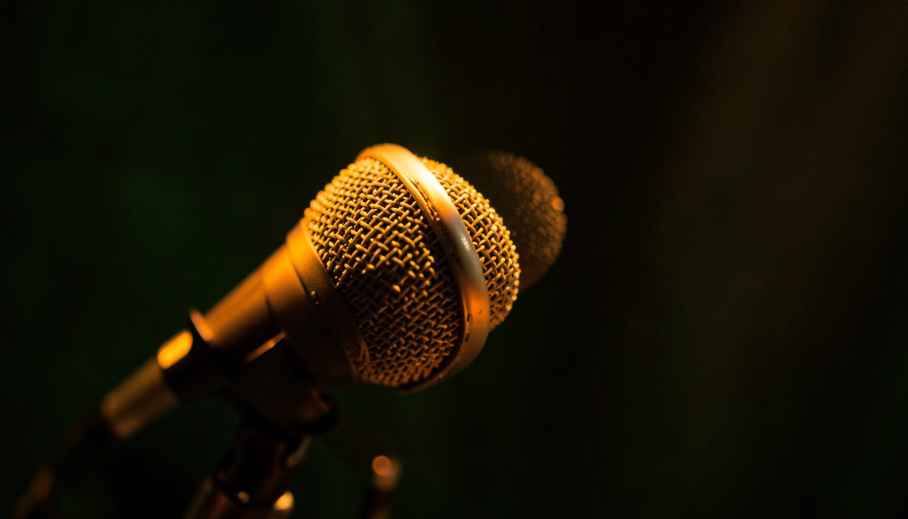 Close-up of a microphone head lit with warm golden light against a dark background, moody atmosphere