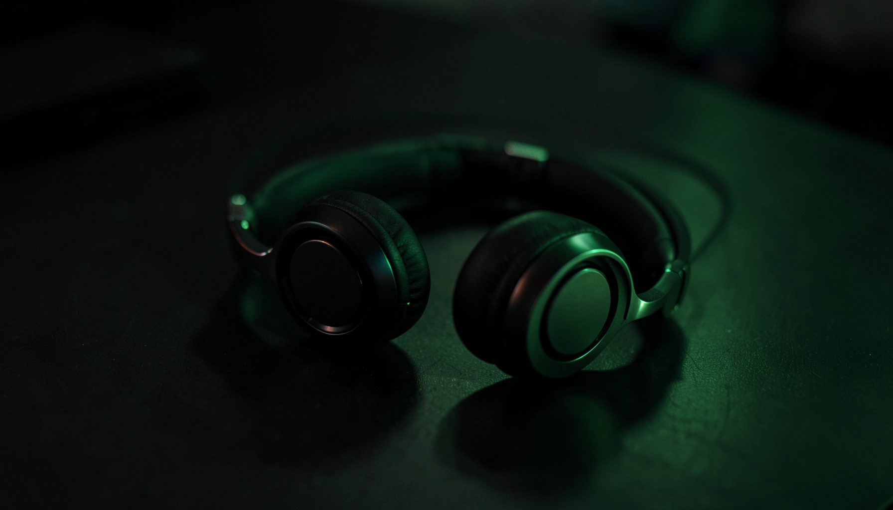 Close-up of black headphones resting on a surface, lit with green light, moody atmosphere