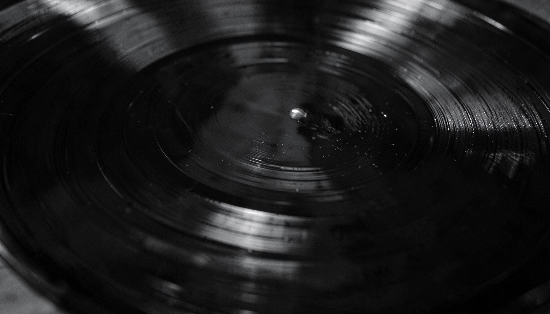 Close-up of a spinning dark vinyl record with reflective concentric grooves, monochrome mood
