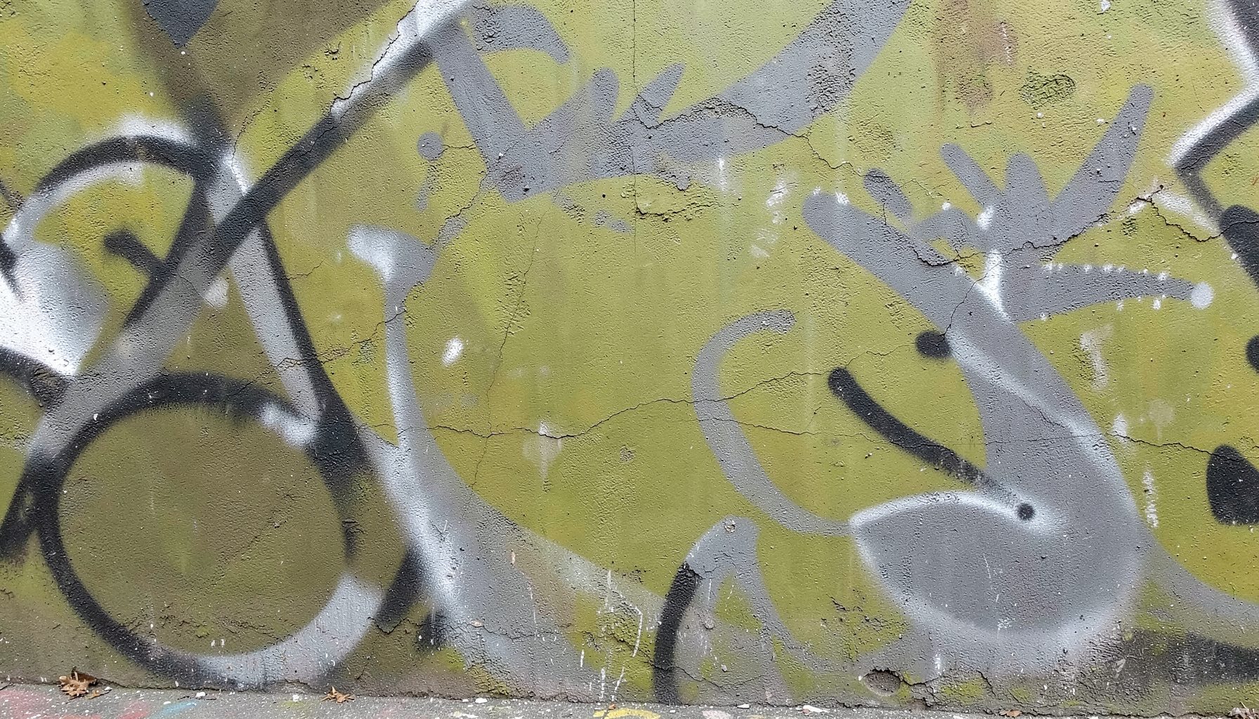 Weathered wall covered in gray and black graffiti over a faded olive green painted surface, gritty urban mood